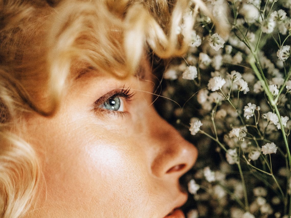 Tekst o budowie, funkcjach, schorzeniach soczewki oka. Na zdjęciu: Kobieta z niebieskimi oczami i zielonymi oczami oraz bukietem kwiatów - HelloZdrowie