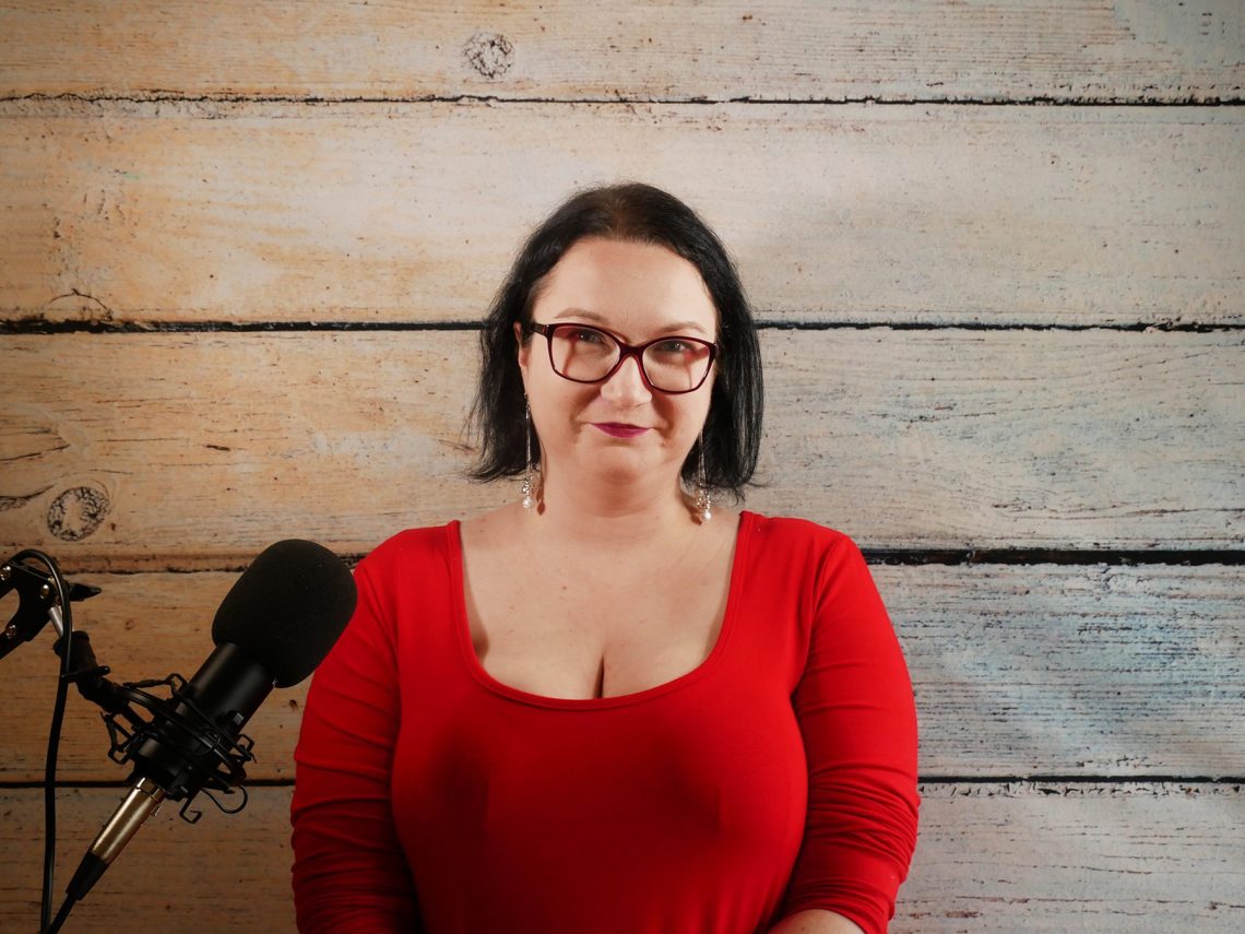 Tekst o mitach i prawdach dotyczących borderline. Na zdjęciu: Kobieta w czerwonej koszuli i okularach stoi przed mikrofonem - HelloZdrowie