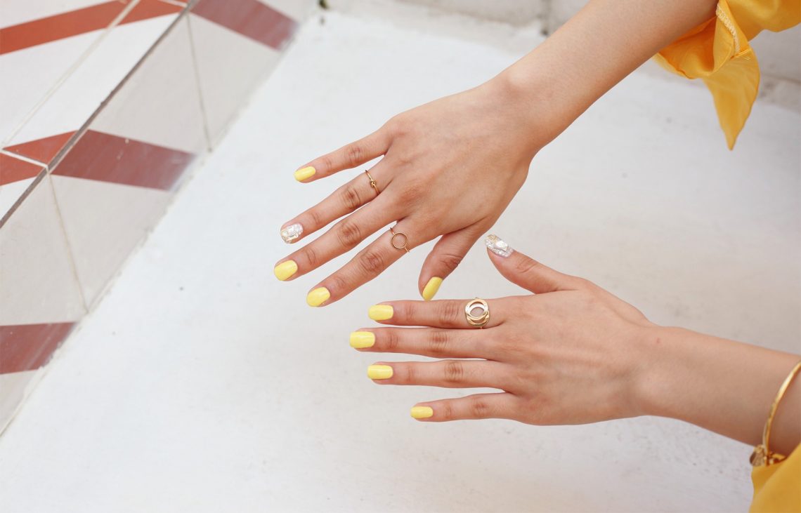 Tekst o lakierze winylowym i jego zastosowaniu. Na zdjęciu: Para rąk z pomalowanymi na żółto paznokciami - HelloZdrowie