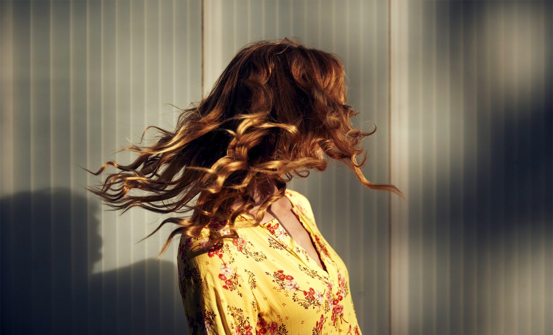 Tekst o rodzajach włosów i ich pielęgnacji. Na zdjęciu: Kobieta z rozpuszczonymi włosami rozwianymi na wietrze - HelloZdrowie