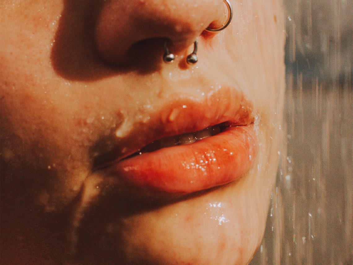 Tekst o samodzielnym wykonaniu i stosowaniu peelingu do ust. Na zdjęciu: Osoba z kolczykiem w nosie pod wodą - HelloZdrowie