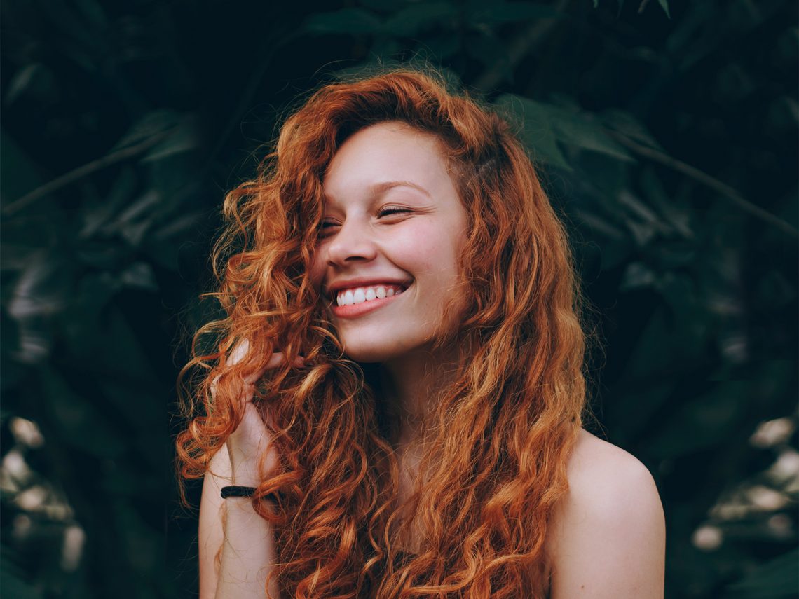 Tekst o rodzajach i zastosowaniach szyn relaksacyjnych. Na zdjęciu: Kobieta uśmiechająca się z długimi rudymi włosami - HelloZdrowie