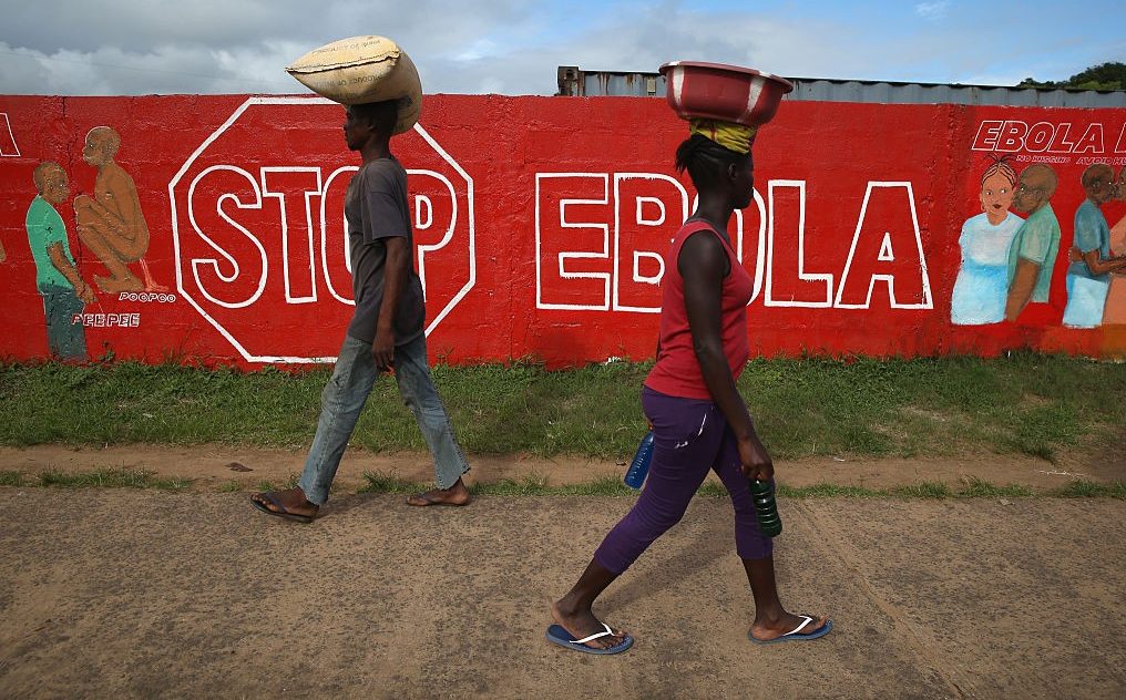 Tekst o zakażeniu wirusem ebola w Wybrzeżu Kości Słoniowej. Na zdjęciu: Mężczyzna i kobieta idący z torbami na głowach - HelloZdrowie