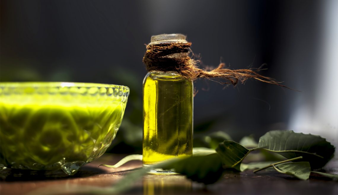 Tekst o właściwościach i zastosowaniu olejku neem. Na zdjęciu: Butelka oleju obok miseczki z zieloną cieczą - HelloZdrowie