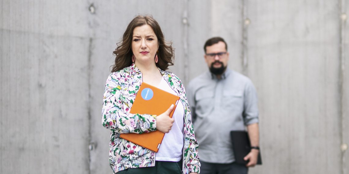 Tekst o wyzwaniach i dobrostanie polskich doktorantów. Na zdjęciu: Kobieta trzymająca folder, z mężczyzną za nią - HelloZdrowie
