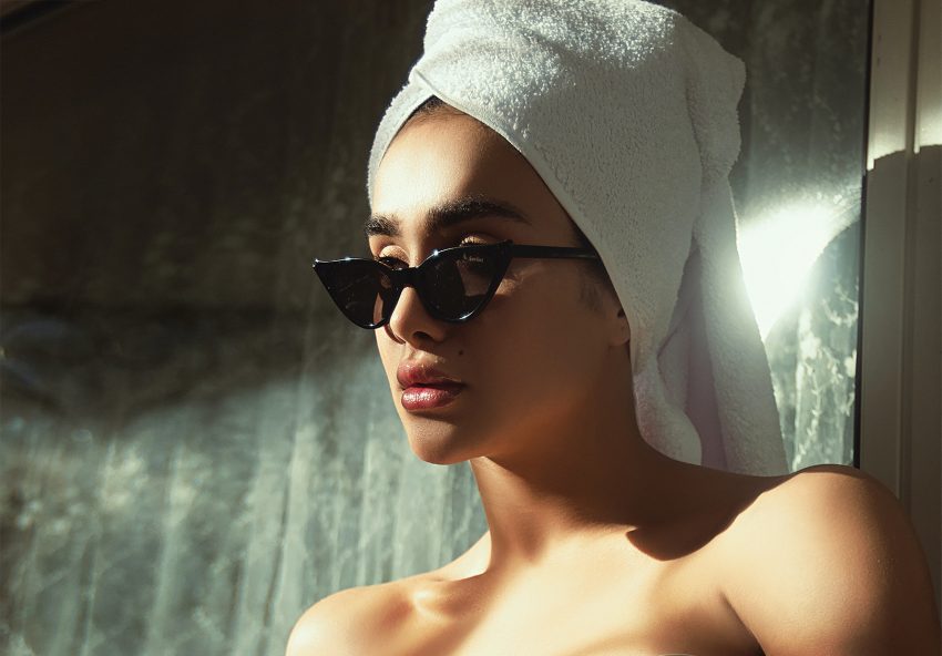 Kobieta z ręcznikiem na głowie. Na twarzy ma okulary przeciwsłoneczne