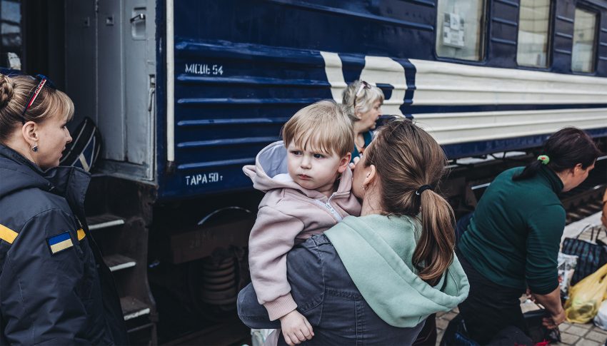 Matka trzyma na rękach dziecko. Stoją przed pociągiem