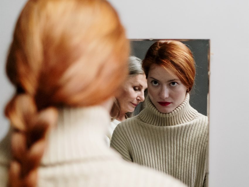 Kobieta przegląda się w lustrze. W odbiciu widać także jej matkę