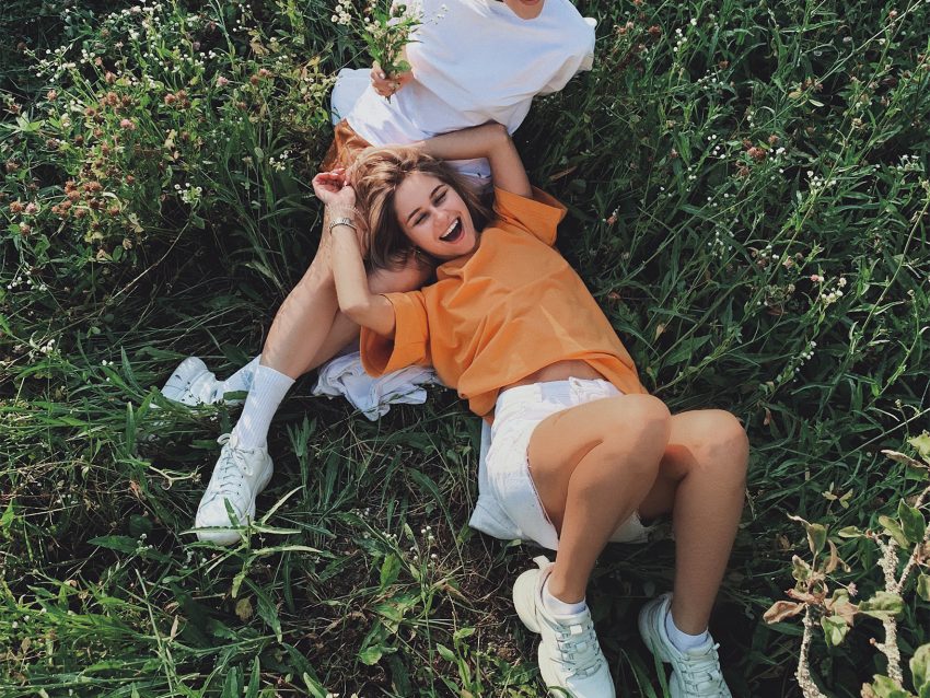 Dwie kobiety leżą na trawie, śmieją się.