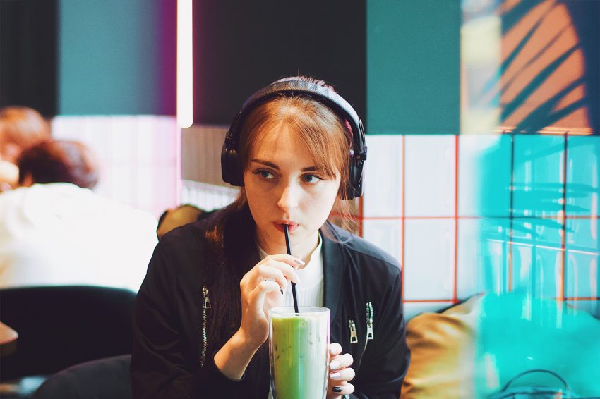 Kobieta siedzi w kawiarni i pije koktajl. Na głowie ma słuchawki.