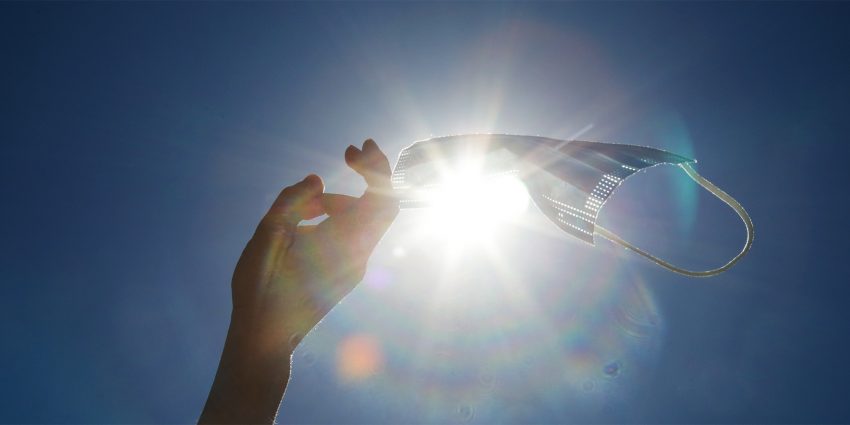 Na zdjęciu ręka rzucająca maseczką w promieniach słońca - HelloZdrowie