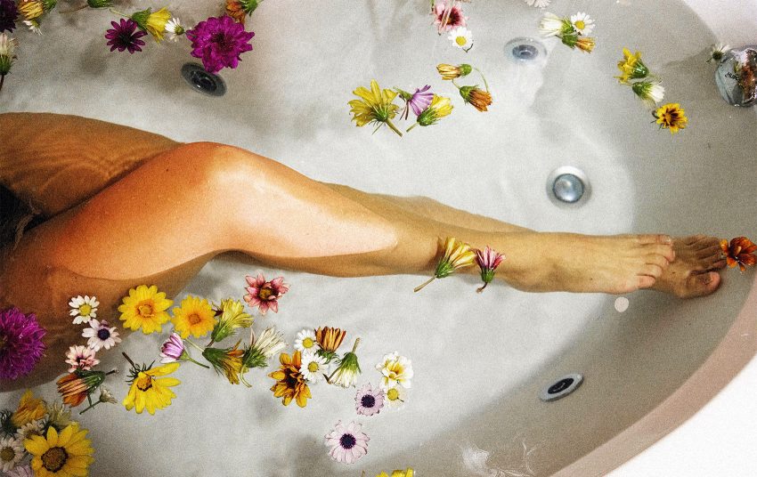 Na zdjęciu kobieca noga w wannie wypełnionej wodą i płatkami kwiatów- HelloZdrowie