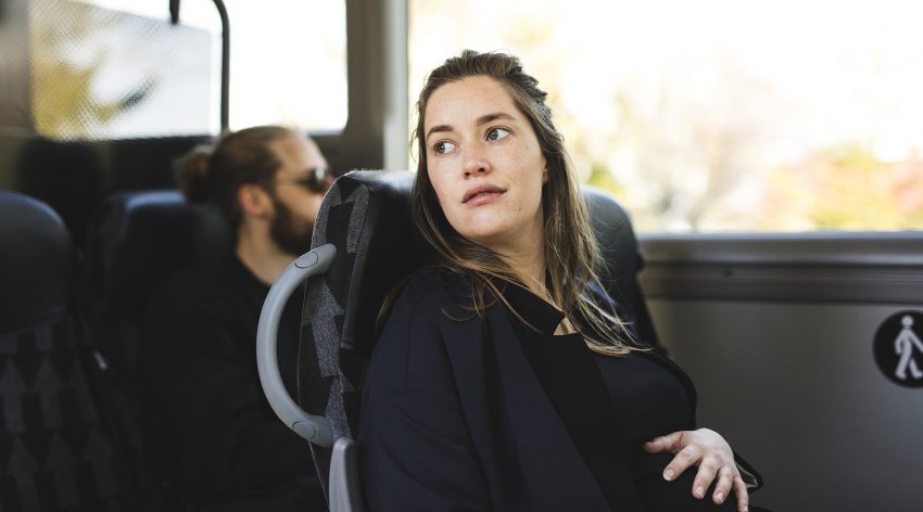 Na zdjęciu siedząca kobieta w ciąży w komunikacji miejskiej, patrząca w dal- HelloZdrowie