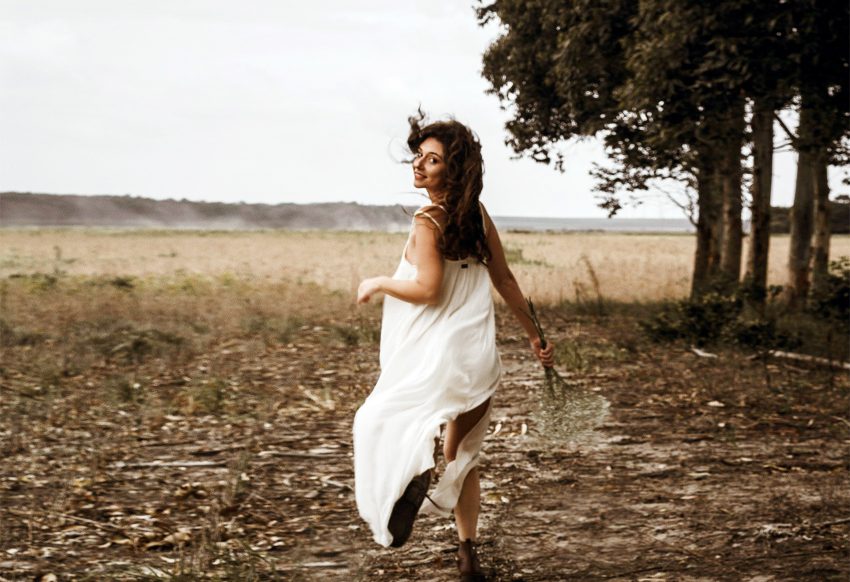 Naturalna kobieta w białej zwiewnej sukience biegnie po polu, zdjęcie w kolorach sepii