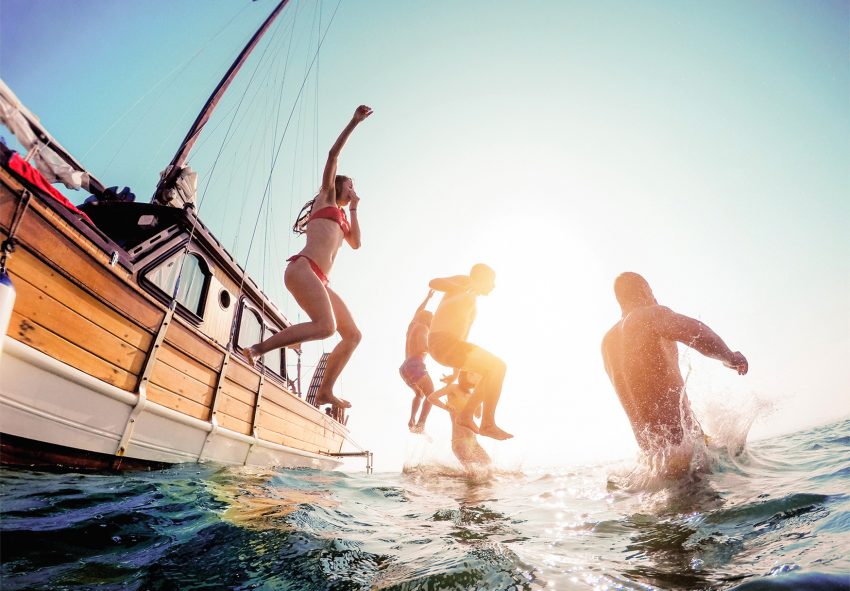 Na zdjęciu młodzi ludzie skaczą do wody z łódki- HelloZdrowie