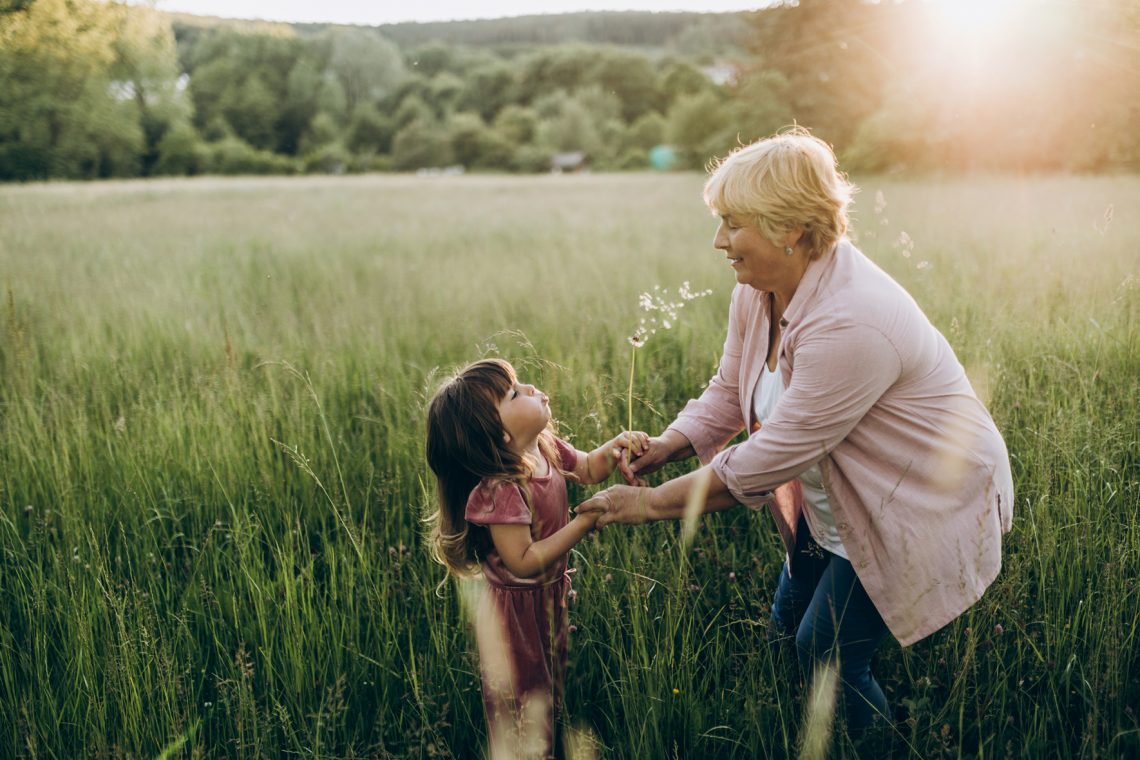 Babcia z wnuczką trzymają się za ręce i bawią na łące