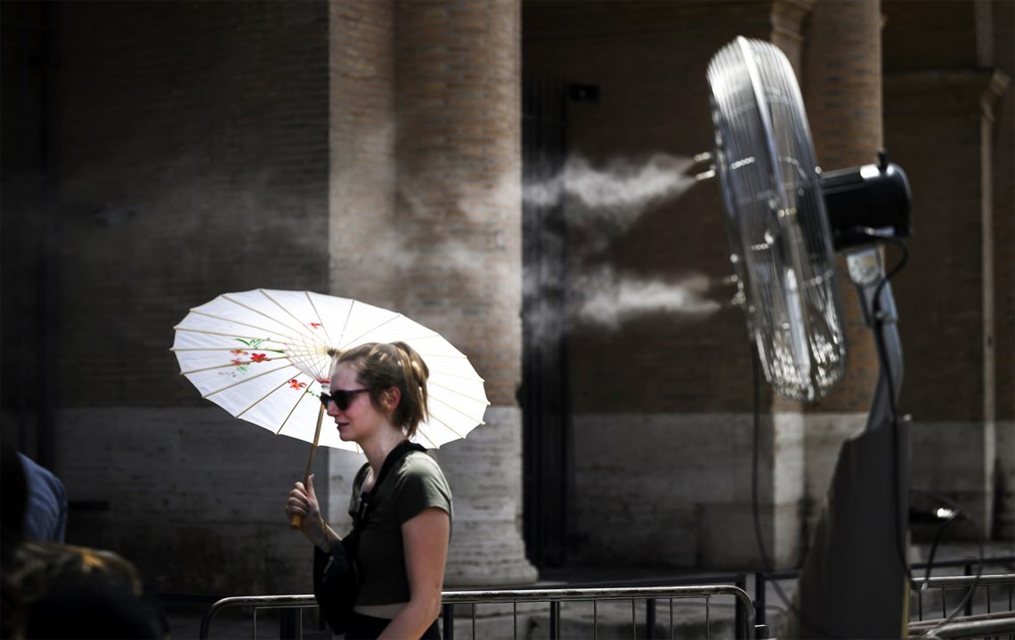 Na zdjęciu kobieta z parasolką, która chroni ją przed słońcem. Za nią wiatrak- HelloZdrowie