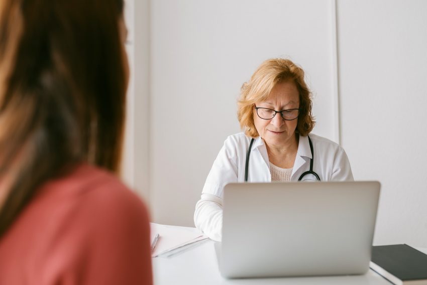 Kobieta na wizycie lekarskiej. Ginekolożka siedzi przy biurku i pisze na laptopie