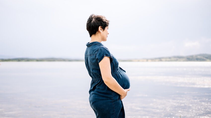 Krótkoobcięta kobieta w ciąży stoi nad brzegiem morza
