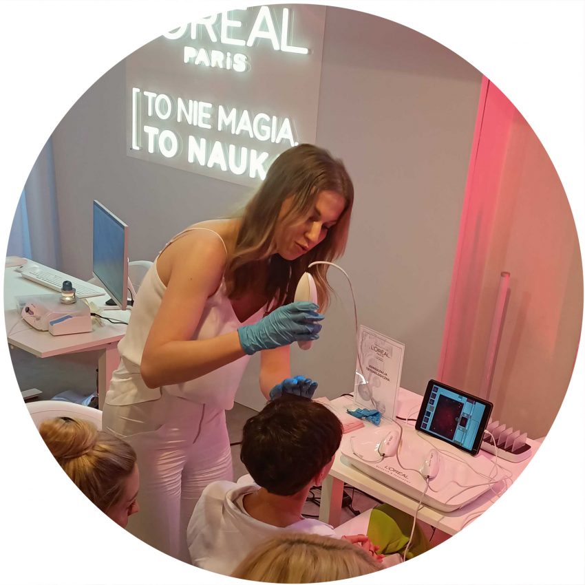 Magdalena Szymczak-Kępka w trakcie przeprowadzania badania skóry głowy - ekspertka przykłada kamerę trychologiczną do skóry głowy pacjentki,