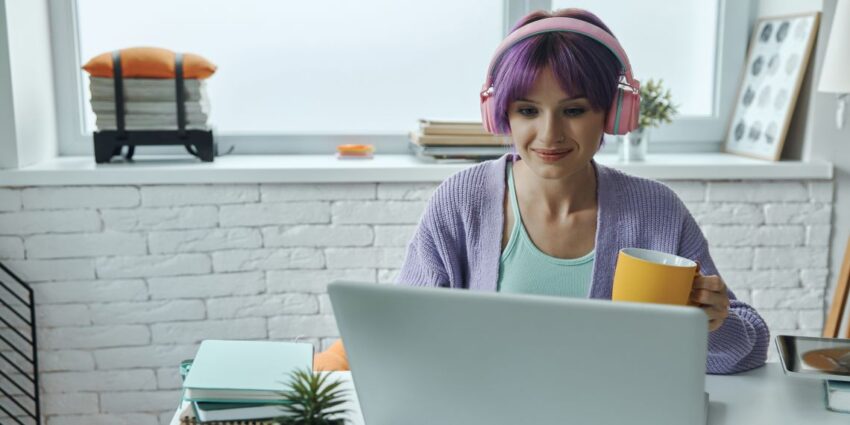 Na zdjęciu kobieta przy laptopie, ze słuchawkami na uszach- HelloZdrowie