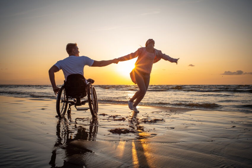 Mężczyzna na wózku inwalidzkim ze swoją partnerką nad brzegiem morza o zachodzie słońca