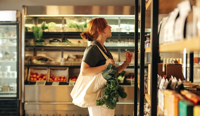 Wegetarianizm mamy zapisany w genach - tak twierdzą norwescy naukowcy - na zdjęciu młoda kobieta robi zakupy, na ramieniu trzyma bawełnianą torbę, z której wystają zielone warzywa HelloZdrowie