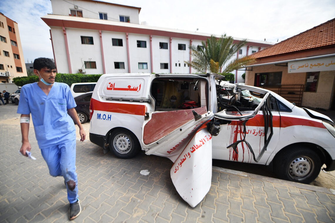 Na zdjęciu uszkodzona pociskiem karetka i idący przed nią lekarz. Zdjęcie ze Strefy Gazy- HelloZdrowie