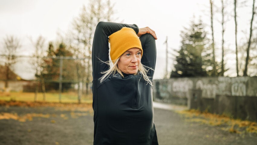 Kobiety objawy zawału mylą z menopauzą - na zdjęciu kobieta w czarnym sportowym ubraniu, żółtej czapce wykonuje serię ćwiczeń na zewnątrz HelloZdrowie