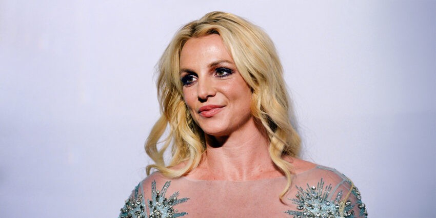 Britney Spears wydała swoją autobiografię "Kobieta, którą jestem" - na zdjęciu pozuje w cekinowej sukience, ma blond kręcone włosy, mocno podkreślony makijaż oczu, delikatny uśmiech HelloZdrowie