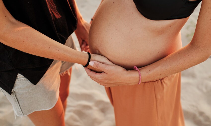 Na zdjęciu kobieta w ciąży trzyma się za ręce z inną kobietą