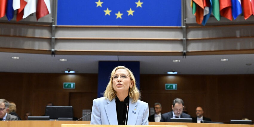 Cate Blanchett apeluje do polityków w Parlamencie Europejskim - na zdjęciu aktorka przemawia ubrana w czarną koszulę i błękitną marynarkę Hello Zdrowie