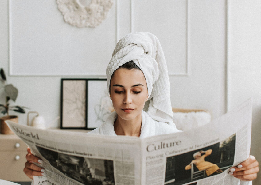 Na zdjęciu kobieta w turbanie z ręcznika, czytająca gazetę- HelloZdrowie