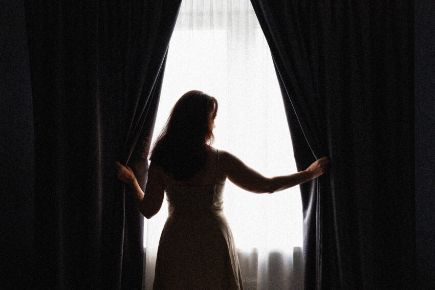 Na zdjęciu kobieta patrząca w okno- HelloZdrowie