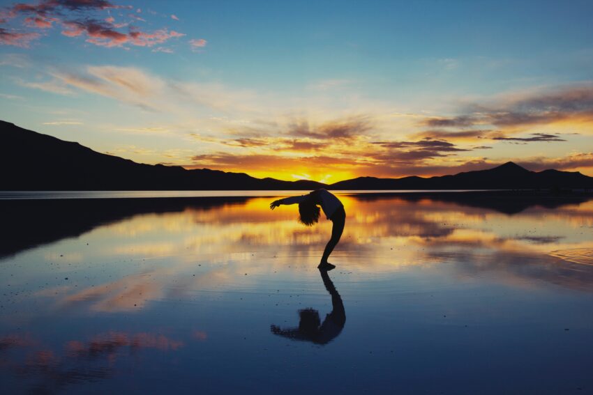 Na zdjęciu kobieta ćwicząca jogę o zachodzie słońca