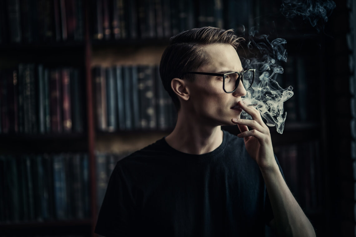 Na zdjęciu młody mężczyzna pali papierosa w salonie z książkami- Hello Zdrowie
