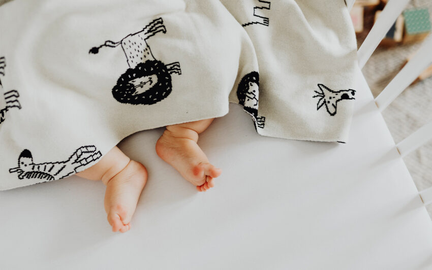 Naukowcy i lekarze ustalili, co może być przyczyną nagłej śmierci łóżeczkowej dzieci - na zdjęciu stopy niemowlaka wystające spod kocyka Hello Zdrowie