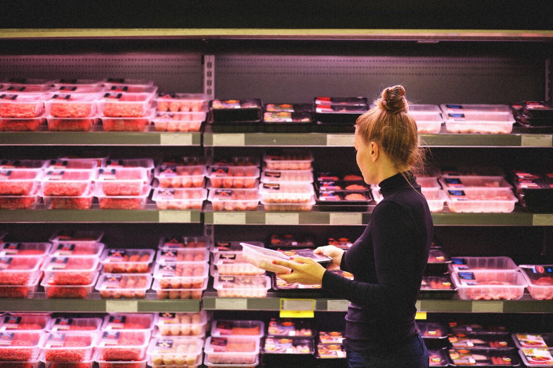 Kobieta w sklepie stoi przed półką z mięsem