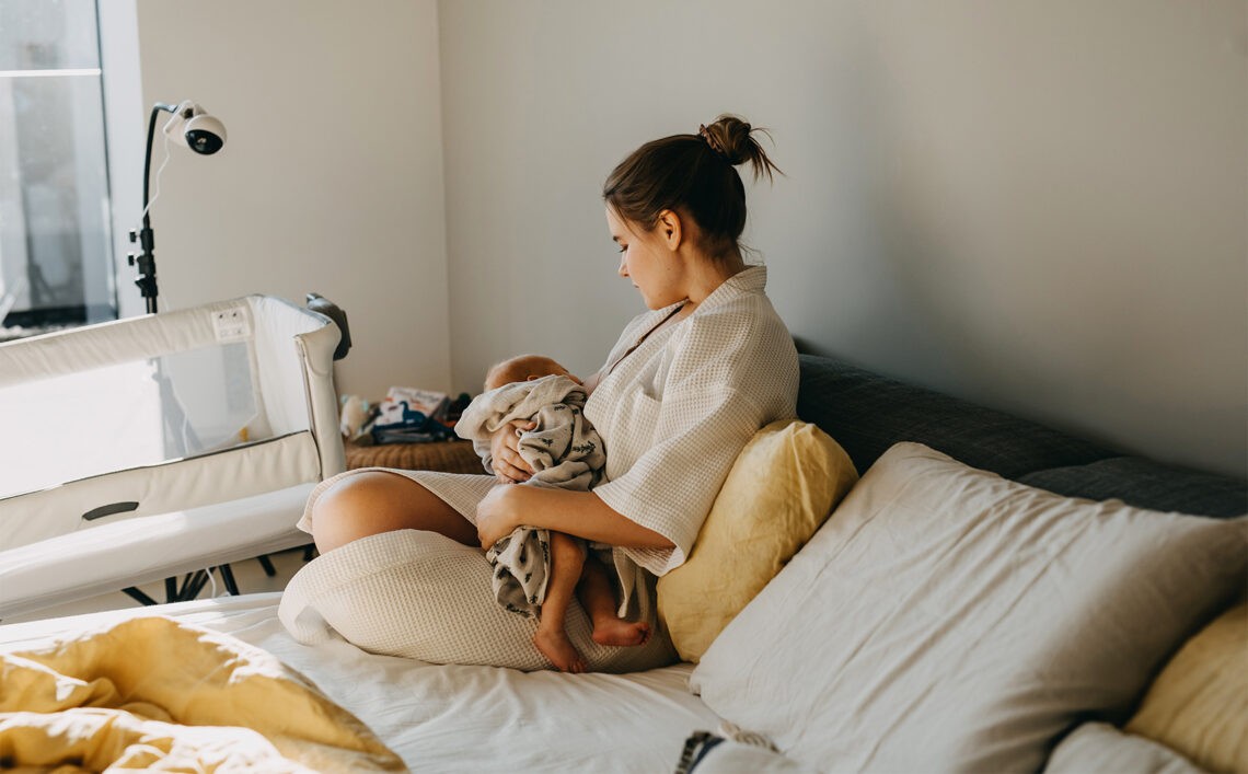 Kobieta siedząca na kanapie i tuląca noworodka- Hello Zdrowie