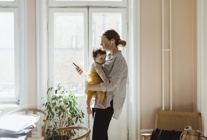Matka z dzieckiem na rękach, ze słuchawkami w uszach i telefonem w dłoni