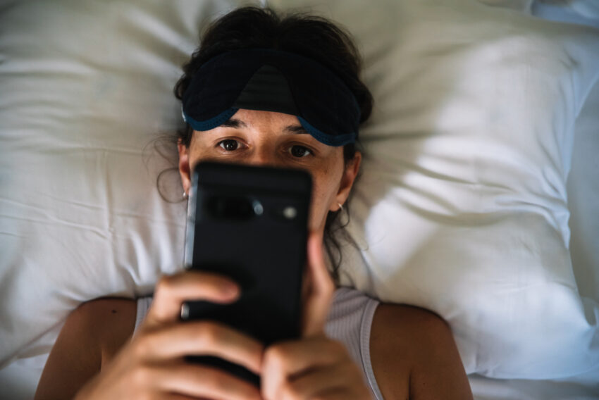 na zdjęciu: kobieta leży w łóżku i patrzy na ekran smartfona, tekst o: popcornowym mózgu /fot. Getty Images