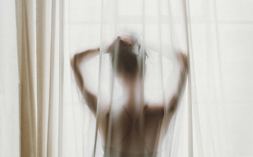 Puchnięcie przed okresem – dlaczego go doświadczasz? ; na zdjęciu kobieta na tle okna- Hello Zdrowie