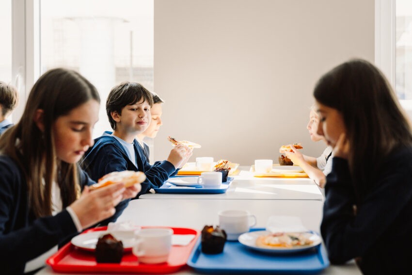 Uczniowie siedzą na szkolnej stołówce i jedzą lunch
