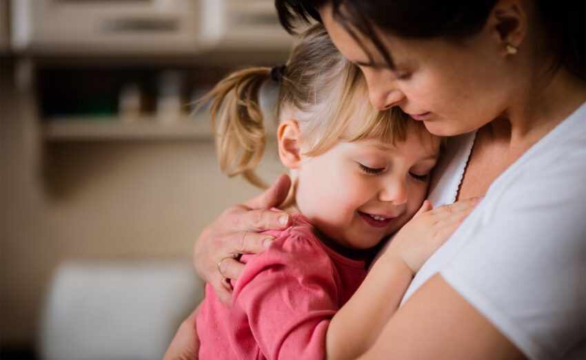 Opieka na dziecko 2024 - na jaką pomoc mogą liczyć rodzice; na zdjęciu mała dziewczynka przytulająca się do mamy- Hello Zdrowie