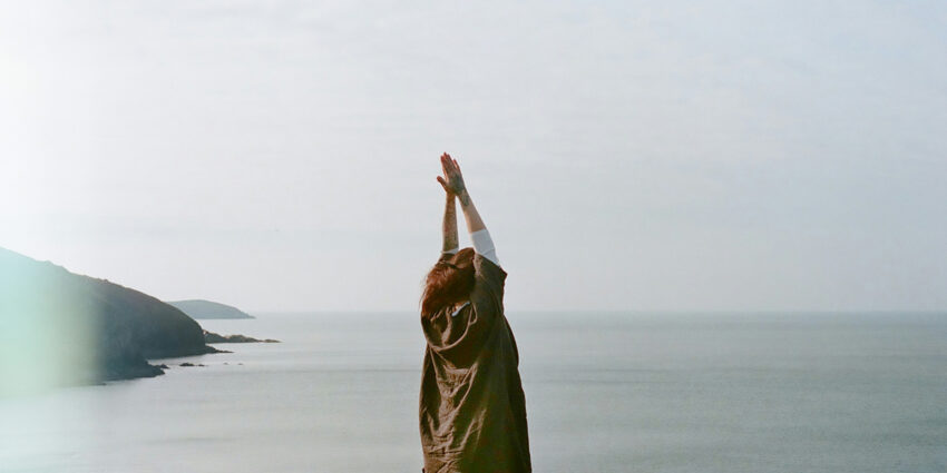 Kobieta uprawia jogę nad brzegiem oceanu. Tekst poświęcony ksiące „Uważność. Trening mindfulness na co dzień”