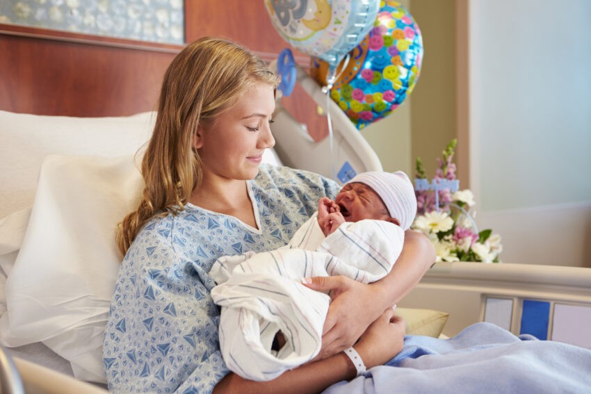 Kobieta leży na szpitalnym łóżku i trzyma niemowlę na rękach