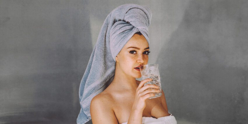 Kobieta z ręcznikiem na głowie i szklanką wody w dłoni