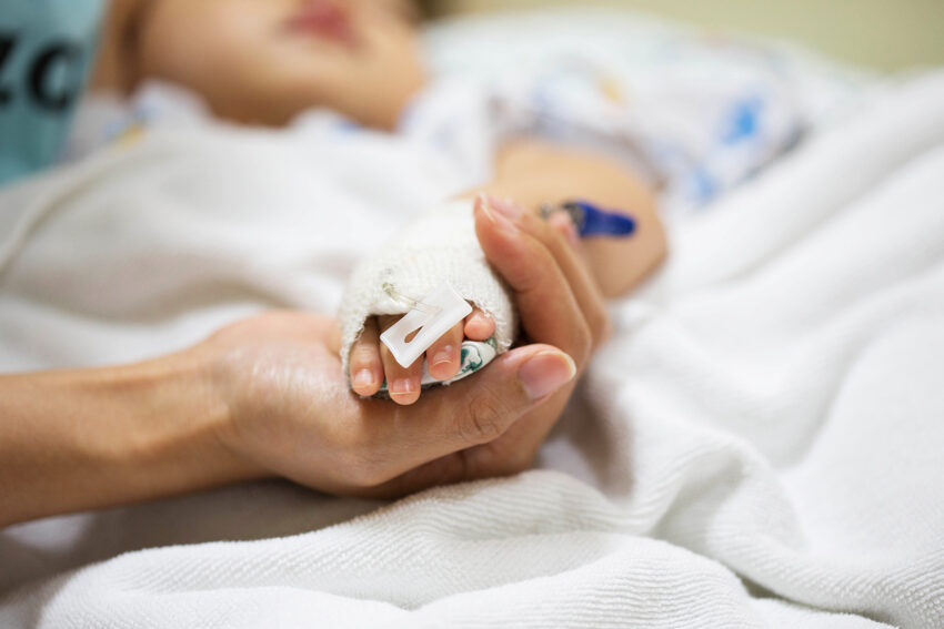 Dorosły trzyma w ręku dłoń hospitalizowanego dziecka