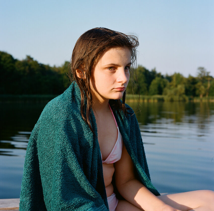 na zdjęciu: dziewczynka w kostiumie kąpielowym siedzi na pomoście, tekst o wystawie "Przypływ" /fot. Magdalena Malinowska