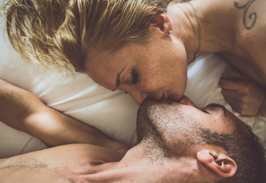 na zdjęciu: para całuje się leżąc w łóżku, tekst o tym, czemu służy całowanie się /fot. Adobe Stock